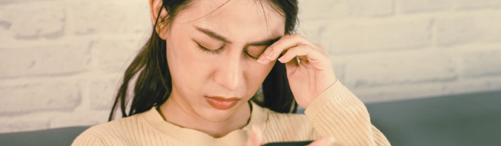 Frau, die sich vor dem Handy die Augen reibt