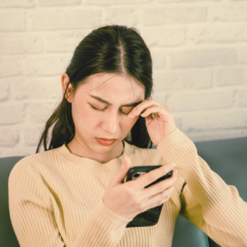 Frau, die sich vor dem Handy die Augen reibt